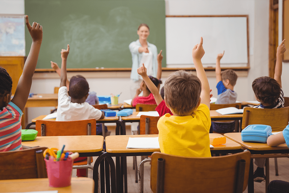 Teacher in front of students with their hands raised